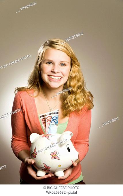 Teenage girl holding piggy bank with money