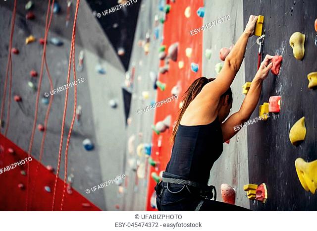 Sporty young woman training in a colorful climbing gym. Free climber girl climbing up indoor