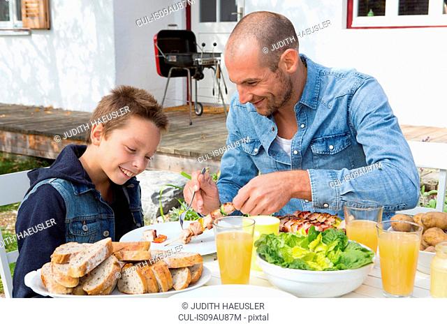 Father and son at garden barbecue table