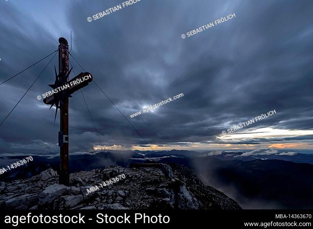 The summit cross of the Guffert in the Brandenberg Alps in Tyrol at the Achensee at sunset and bad weather in summer