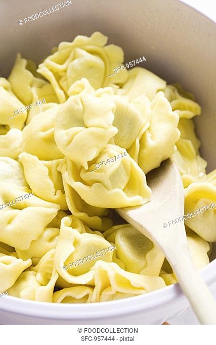 Tortellini in white bowl with wooden spoon detail