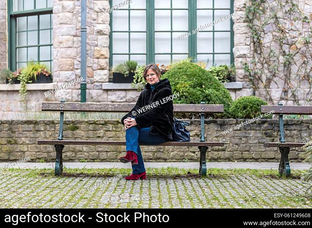 Fashionable white woman sitting on a bench with an historic building in the background, Brussels old town, Belgium