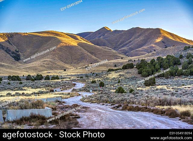 Winding road and huge mountain in Utah Valley. A winding road on a terrain covered with shrubs in Utah Valley with view of an immense mountain illuminated by...