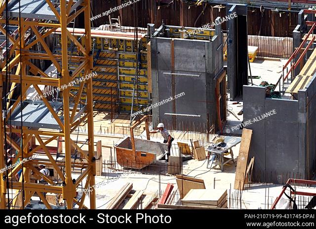 15 July 2021, Brandenburg, Potsdam: A worker directs an empty container within reach of the crane on the construction site between Friedrich-Ebert-Strasse