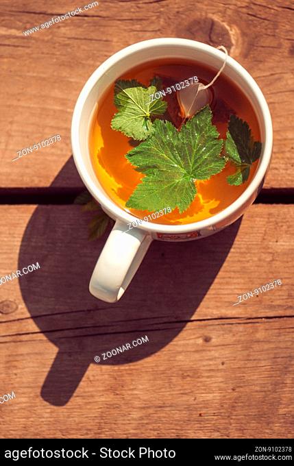 Top view of tea with currant leaf in white cup