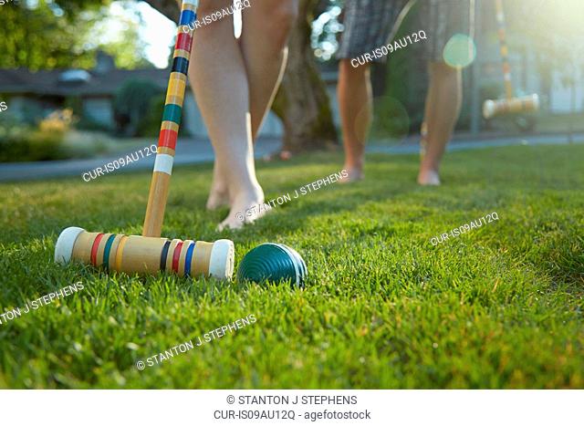 Legs and bare feet of young couple playing croquet on grass