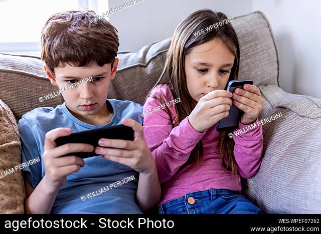 Girl and boy using smart phone on sofa at home
