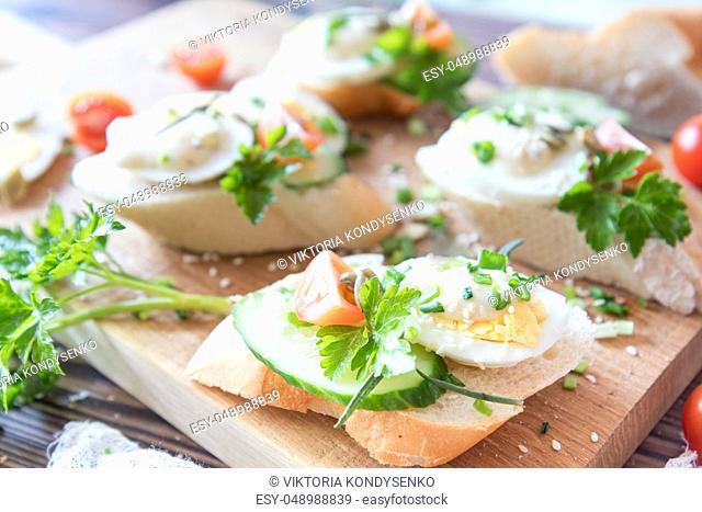 Bread with slices of fresh cucumber, egg, tomato and cream cheese on a wooden cutting board. Fresh parsley and rosemary