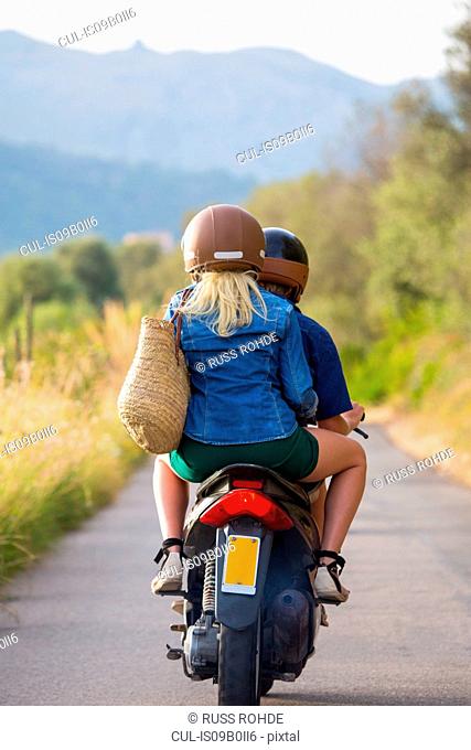 Rear view of young couple riding moped on rural road, Majorca, Spain
