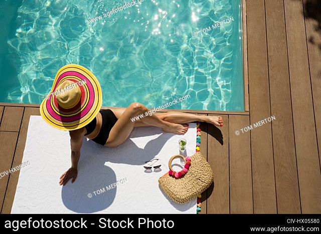 Woman in sun hat sunbathing, relaxing at sunny summer poolside