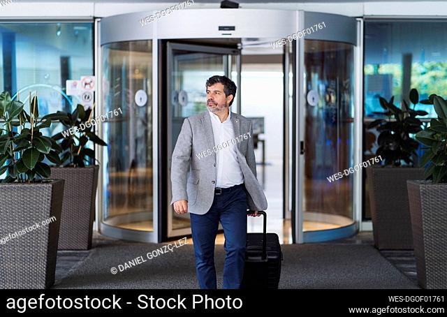 Confident businessman pulling wheeled luggage while entering hotel