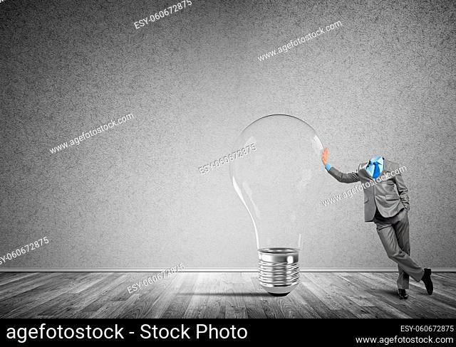 Headless businessman in empty room leaning on glass light bulb