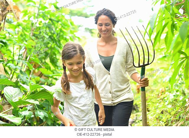 Girl and woman with gardening fork walking through plants in greenhouse