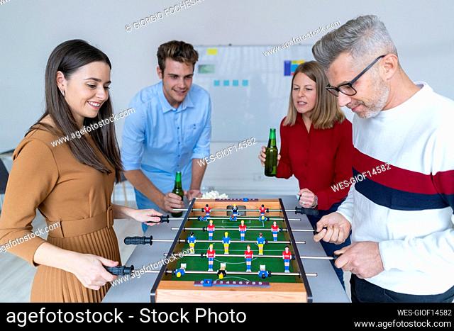 Businesswoman cheering up colleagues playing foosball in office