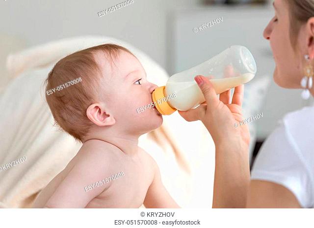 Closeup portrait of baby boy drinking milk from bottle that mother is holding