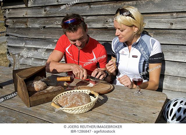 Bicycle racers taking a break with South Tyrolean bacon and wine at the mountain lodge on the Passo di Pennes, South Tyrol, Italy, Europe