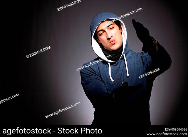 Young gangster in hood on grey background