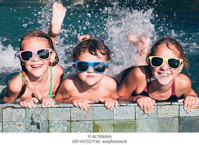Three happy children playing on the swimming pool at the day time. Kid having fun outdoors. Concept of friendly family