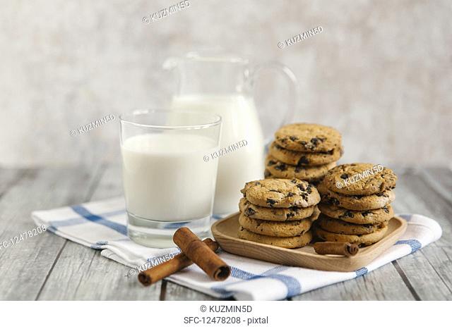 Milk in a jar and a jug, with chocolate chip cookies and cinnamon sticks