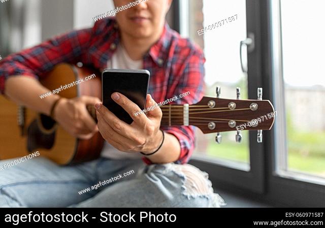 man with guitar and phone sitting on sill