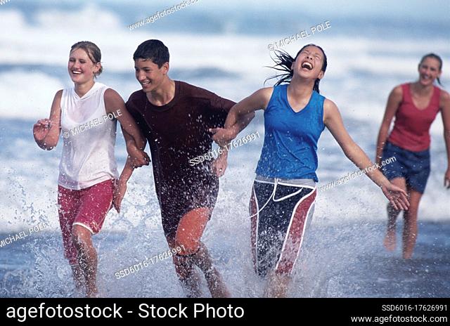 Teenage boy and girls running in the waves at the beach and laughing