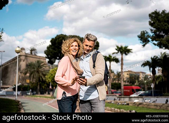 Mature man using smart phone by woman in city