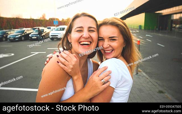 Toned portrait of two smiling and laughing girls friends hugging on car parking at shopping mall