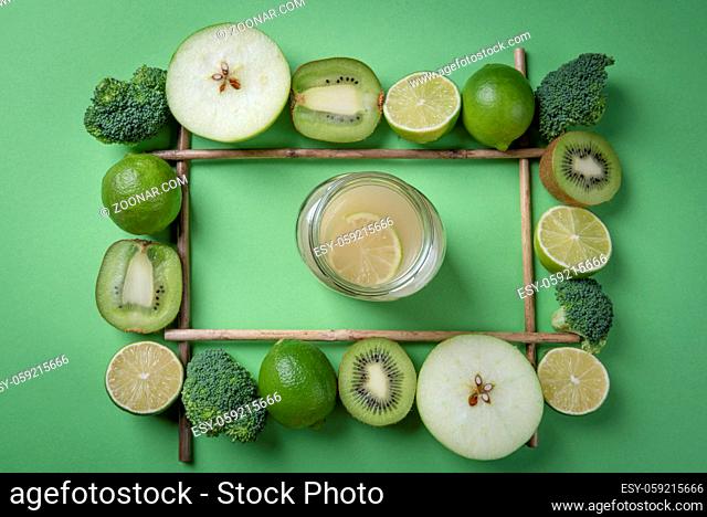 Lemonade in a jar directly above view, surrounded by a frame of green fruits and broccoli. Detoxification food and drink