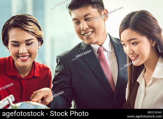 Close-up of young smiling businesspeople looking at globe