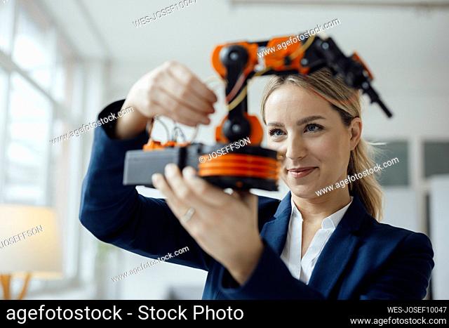 Smiling businesswoman analyzing robotic arm model in office