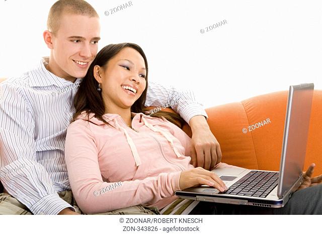 Junges Paar sitzt lachend mit einem Laptop auf dem Sofa und surft im Internet