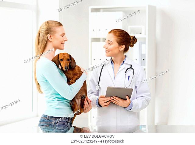 medicine, pet, health care, technology and people concept - happy woman holding dachshund dog and veterinarian doctor with tablet pc computer talking at vet...