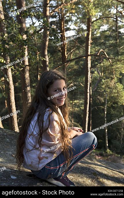 Girl wearing jeans and a shawl, squatting on a flat rock, Rochers d'Angennes site, Forest of Rambouillet, Haute Vallee de Chevreuse Regional Natural Park