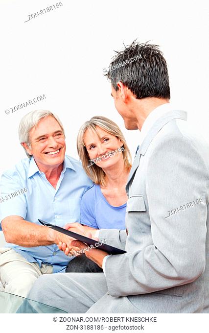 Seniorenpaar begrüßt Anlageberater mit Handschlag im Wohnzimmer