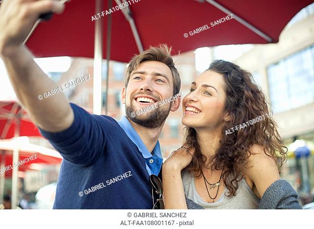 Couple posing for a selfie at an outdoor cafe