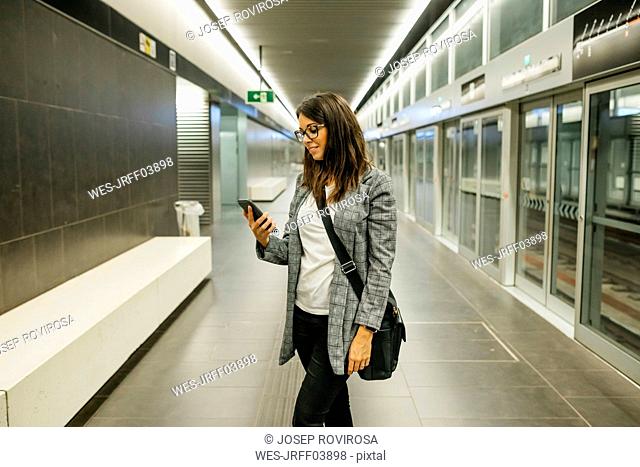 Young businesswoman using the phone at the subway station, waiting for the train