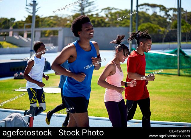 Smiling track and field athletes running on sunny sports track