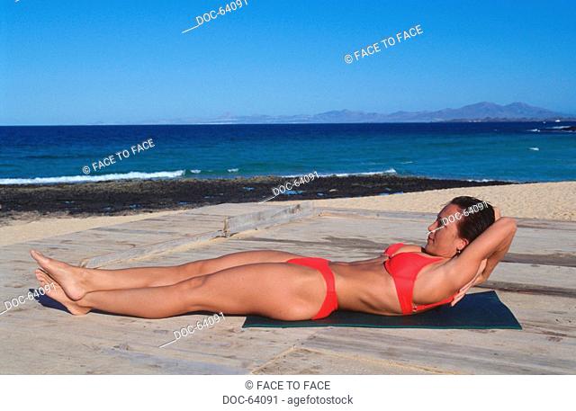 woman does doing sports on a platform at the sea - supine position