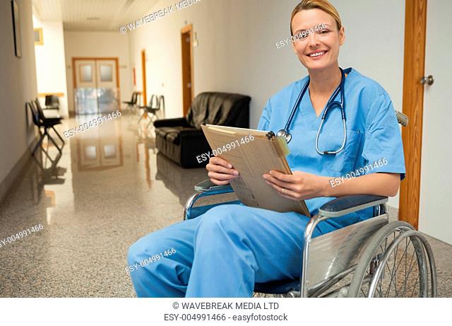Smiling nurse in a wheelchair holding a folder in hospital corridor