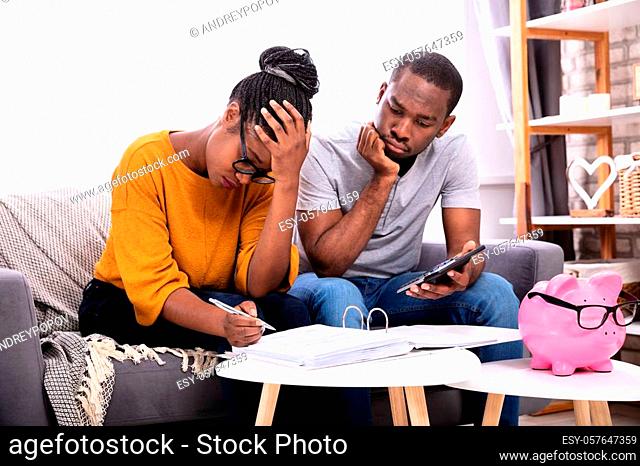 Sad African Couple Sitting On Sofa Examining Bill