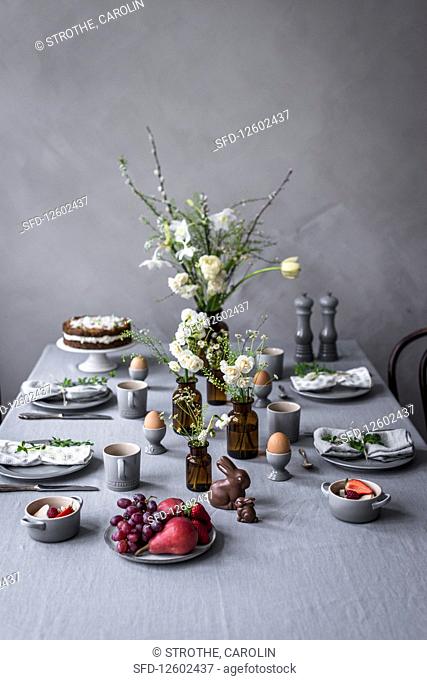 A table laid for an Easter breakfast with boiled eggs, carrot cake, chocolate bunnies and fruit salad