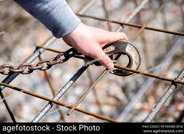 12 April 2022, North Rhine-Westphalia, Hörstel: An employee of a construction company hooks the iron cages for the foundation of a hall onto a crane hook at a...