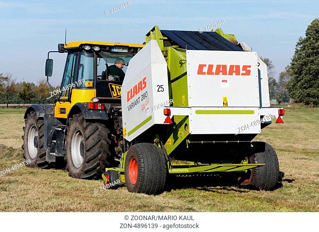 Ein Traktor vom Typ JCB Fastrac 3190 Plus mit einer Rundballenpresse vom Typ CLAAS Variant 280 bei der Heuernte auf einem Feld bei Dautschen in Sachsen