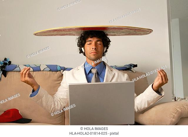 Young man sitting with a laptop in his lap and a body board on his head