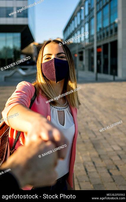 Woman wearing face mask greeting person with a fist bump in the city