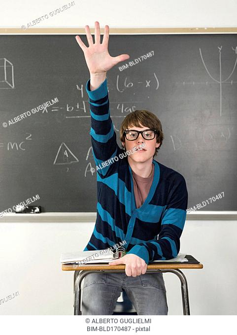 Student raising his hand at desk in classroom