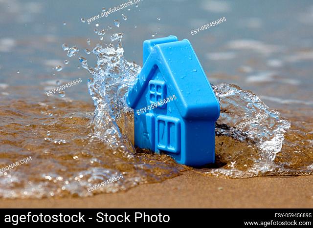 Blue plastic toy house on the sand covered with the waves, forming the spray - a metaphor for the sudden flooding