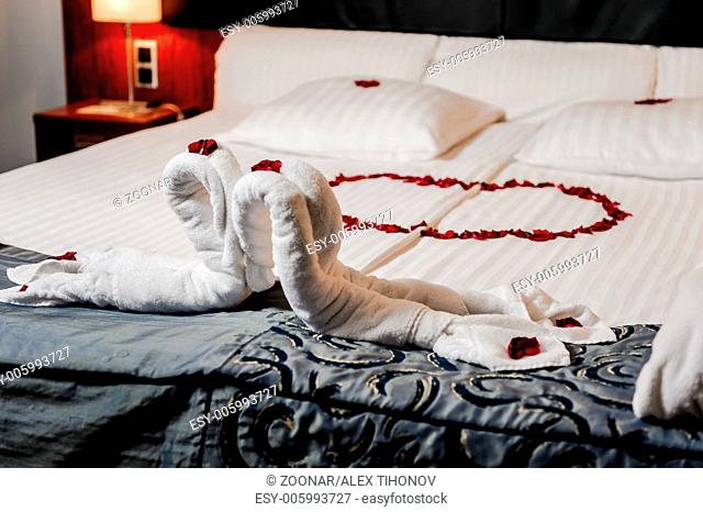 Honeymoon bed decorated with red rose petals and towels