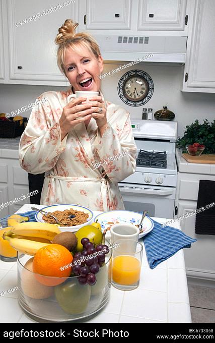 Attractive woman in kitchen with fruit, coffee, orange juice and breakfast bowls