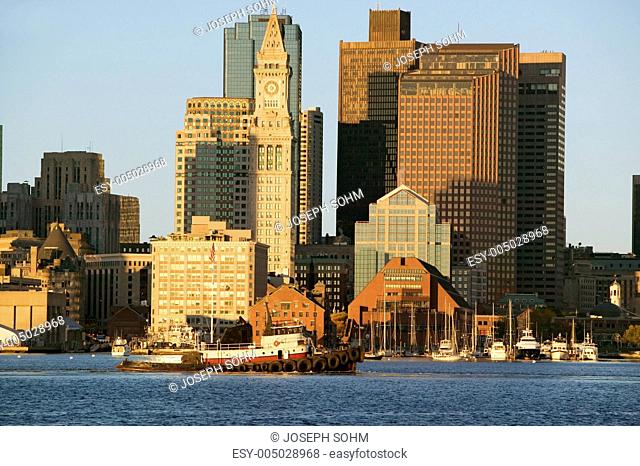 Tugboat with Boston Harbor and the Boston skyline at sunrise as seen from South Boston, Massachusetts, New England